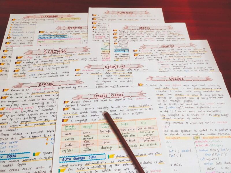 c programming first page with headings of strings, error, unions, storage classes, in sample 6 with pink Highlighters include in photo of physical copy kept on wooden desk